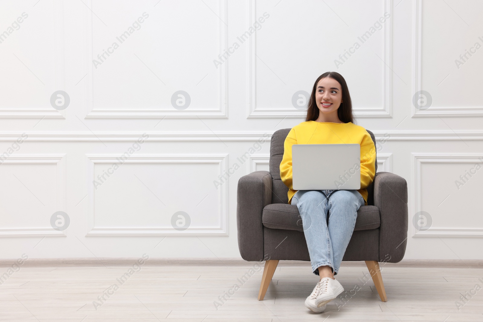 Photo of Beautiful woman with laptop sitting in armchair near white wall indoors, space for text