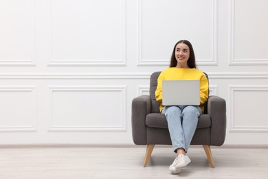 Photo of Beautiful woman with laptop sitting in armchair near white wall indoors, space for text