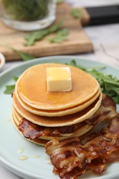 Photo of Tasty pancakes with butter, fried bacon and fresh arugula on white marble table, closeup