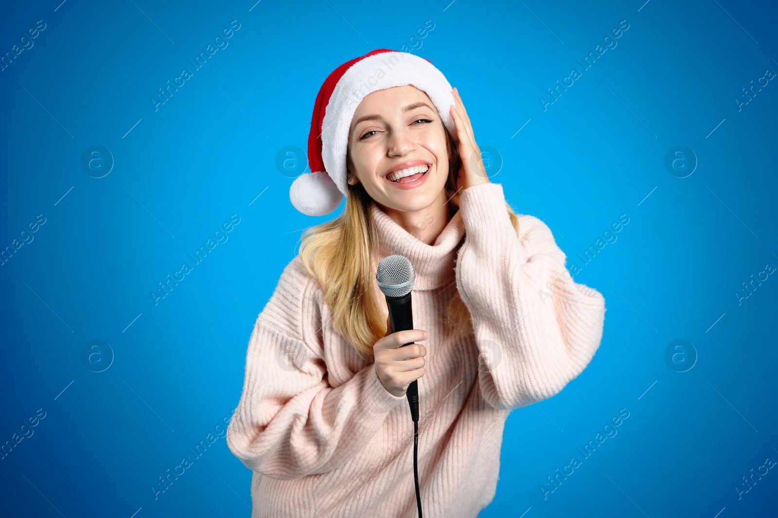 Photo of Happy woman in Santa Claus hat singing with microphone on blue background. Christmas music