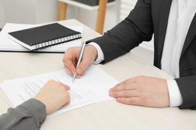 Photo of Woman pointing at document and man putting signature at wooden table, closeup