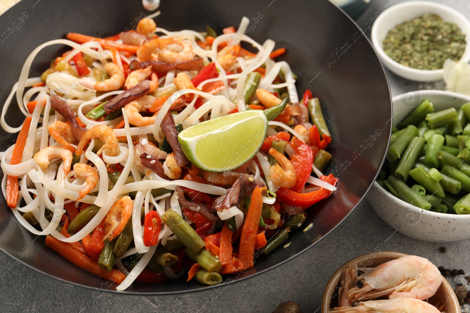 Photo of Shrimp stir fry with noodles and vegetables in wok on grey table, closeup