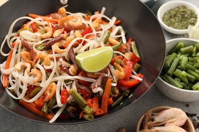 Shrimp stir fry with noodles and vegetables in wok on grey table, closeup