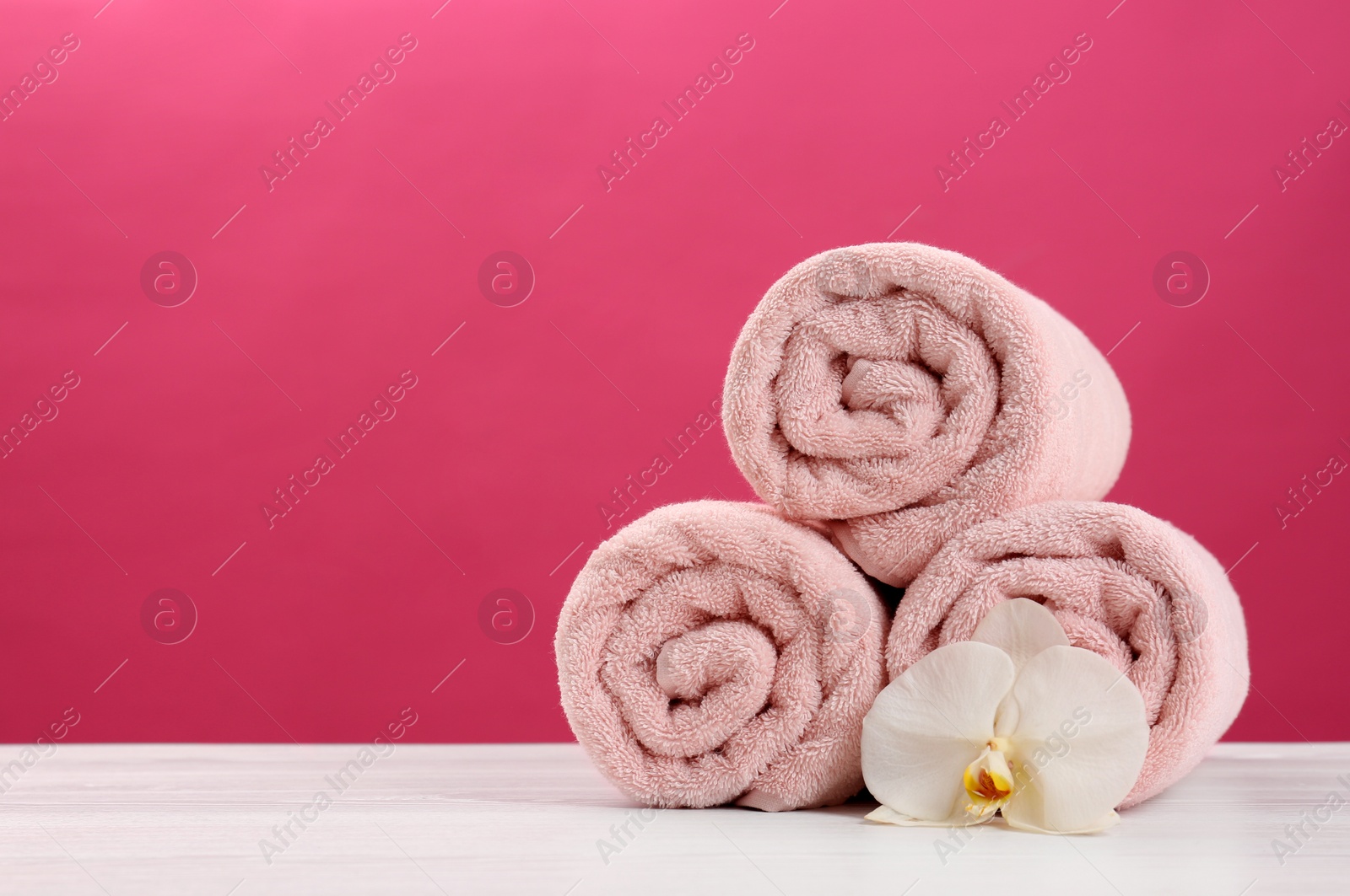 Photo of Rolled soft towels with beautiful flower on table against color background. Space for text