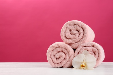 Rolled soft towels with beautiful flower on table against color background. Space for text