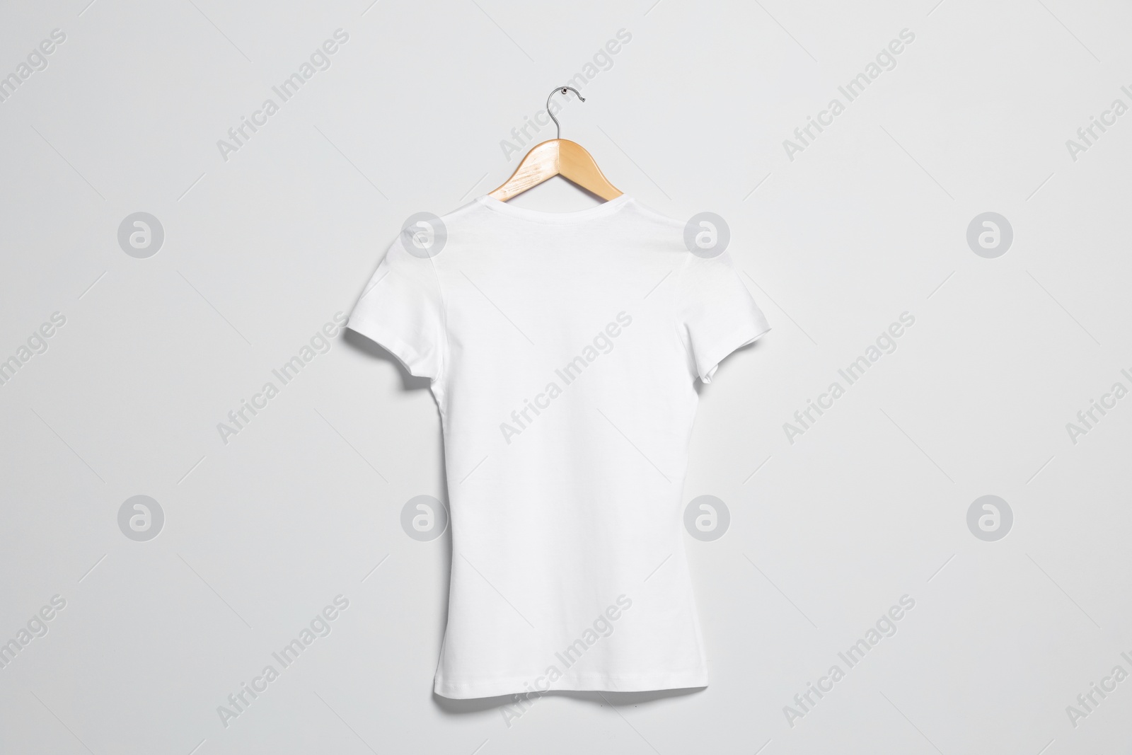 Photo of Hanger with white t-shirt on light wall. Mockup for design