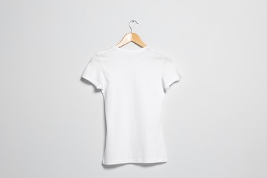 Photo of Hanger with white t-shirt on light wall. Mockup for design