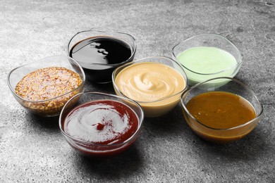 Photo of Many bowls with different sauces on grey table