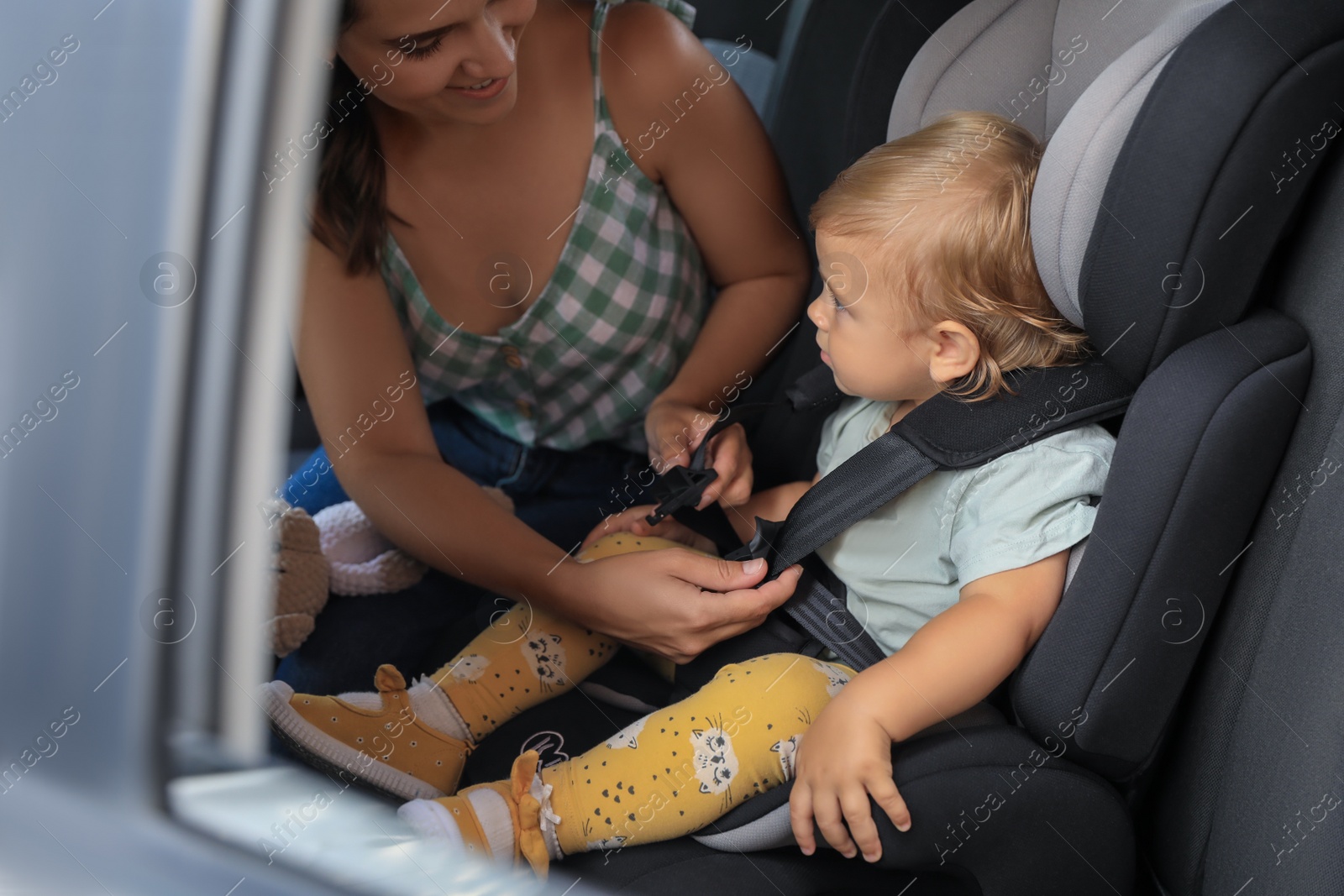 Photo of Mother fastening her daughter in child safety seat inside car