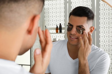 Man applying dark under eye patch near mirror at home