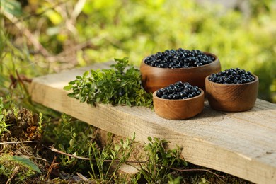 Photo of Delicious bilberries and branch with fresh berries on wooden bench outdoors