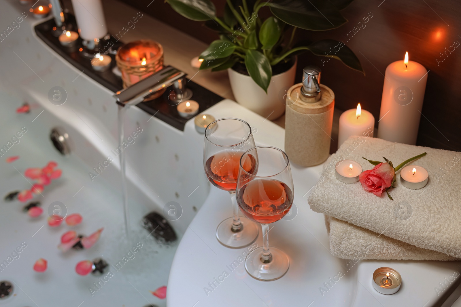 Photo of Bathtub with glasses of wine and candles indoors. Romantic atmosphere