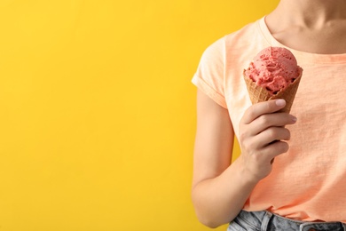 Woman holding pink ice cream in wafer cone on yellow background, closeup. Space for text