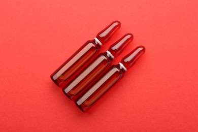 Photo of Glass ampoules with liquid on red background, top view