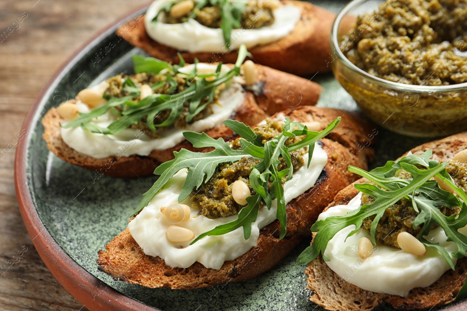 Photo of Plate with tasty bruschettas and pesto sauce on wooden table, closeup