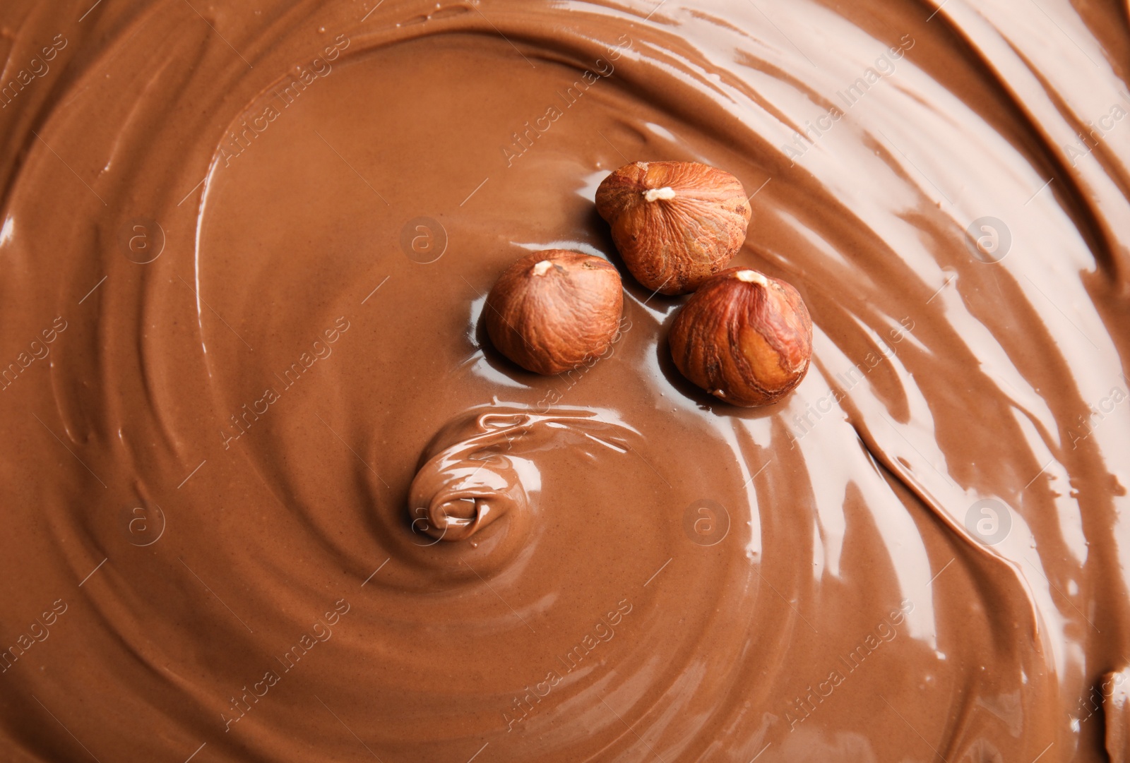 Photo of Sweet tasty chocolate cream with hazelnuts as background, closeup