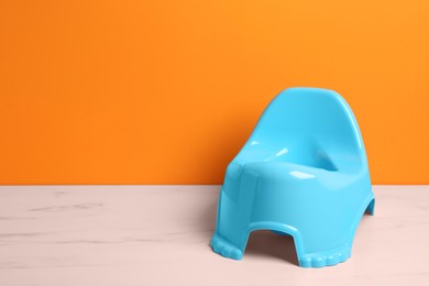 Photo of Light blue baby potty on white marble table against orange background, space for text. Toilet training