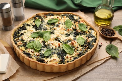 Delicious homemade quiche, fresh spinach leaves and spices on wooden table