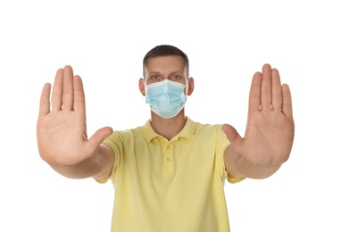 Man in protective mask showing stop gesture on white background. Prevent spreading of coronavirus