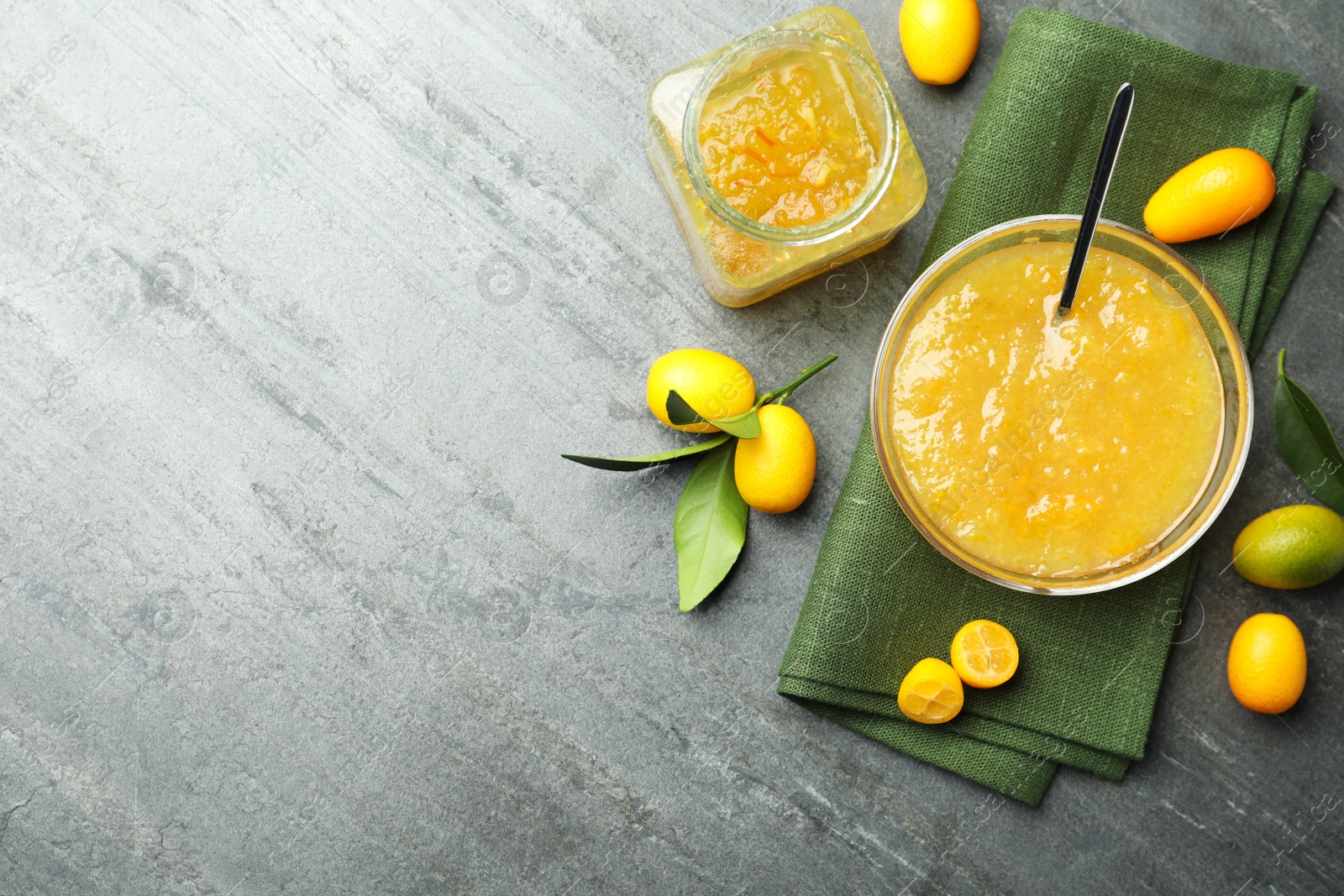 Photo of Delicious kumquat jam in bowl and fresh fruits on grey table, flat lay. Space for text