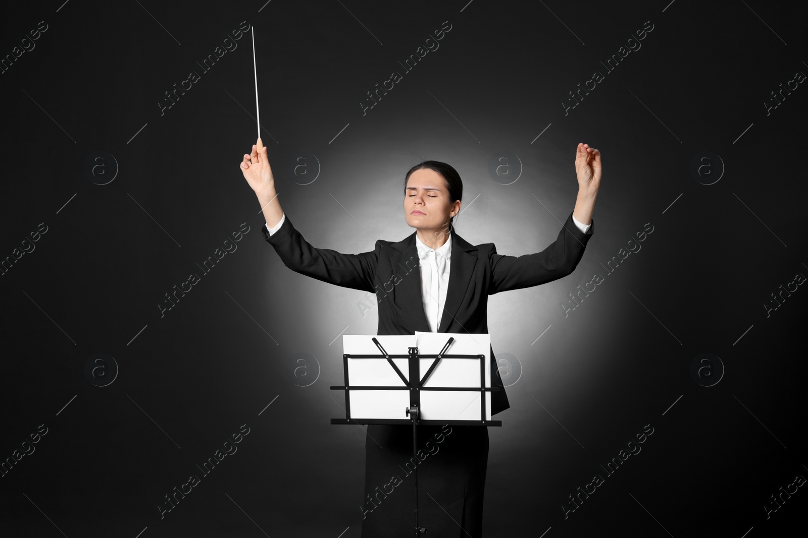 Photo of Professional conductor with baton and note stand on black background