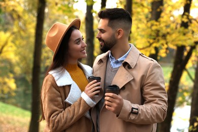 Photo of Happy young couple with cups of coffee spending time together in autumn park