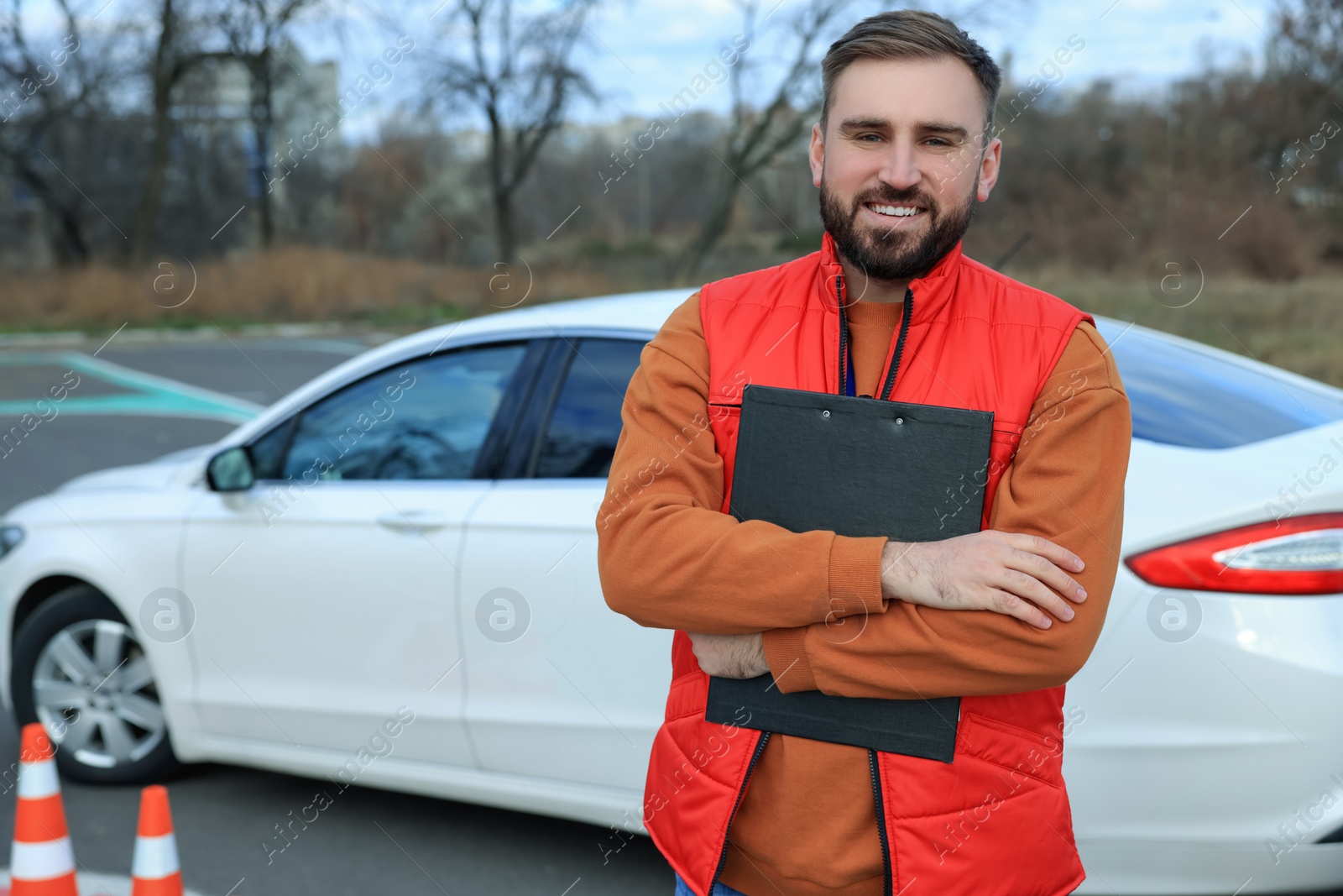 Photo of Instructor with clipboard near car on test track. Driving school