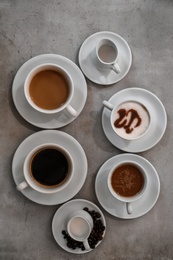 Cups of fresh aromatic coffee on grey background, top view