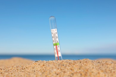 Glass weather thermometer in sand near sea