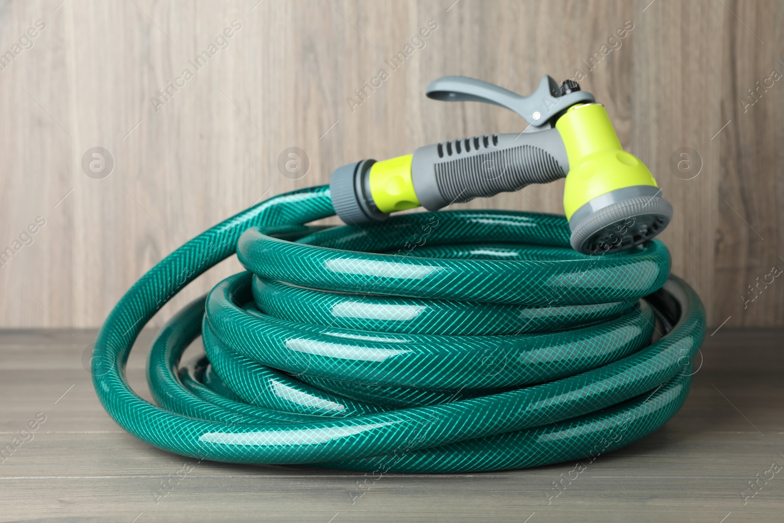 Photo of Green rubber watering hose with nozzle on wooden surface