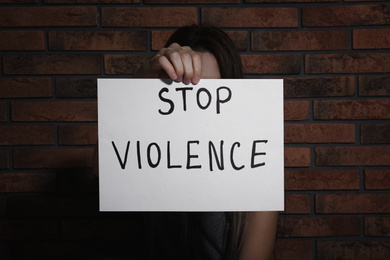 Photo of Young woman with sign STOP VIOLENCE near brick wall