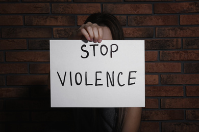 Young woman with sign STOP VIOLENCE near brick wall