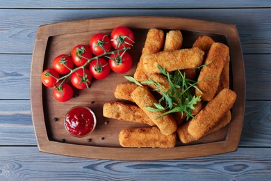 Photo of Board with cheese sticks, sauce and tomatoes on table, top view