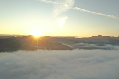 Aerial view of beautiful mountains covered with fluffy clouds at sunrise