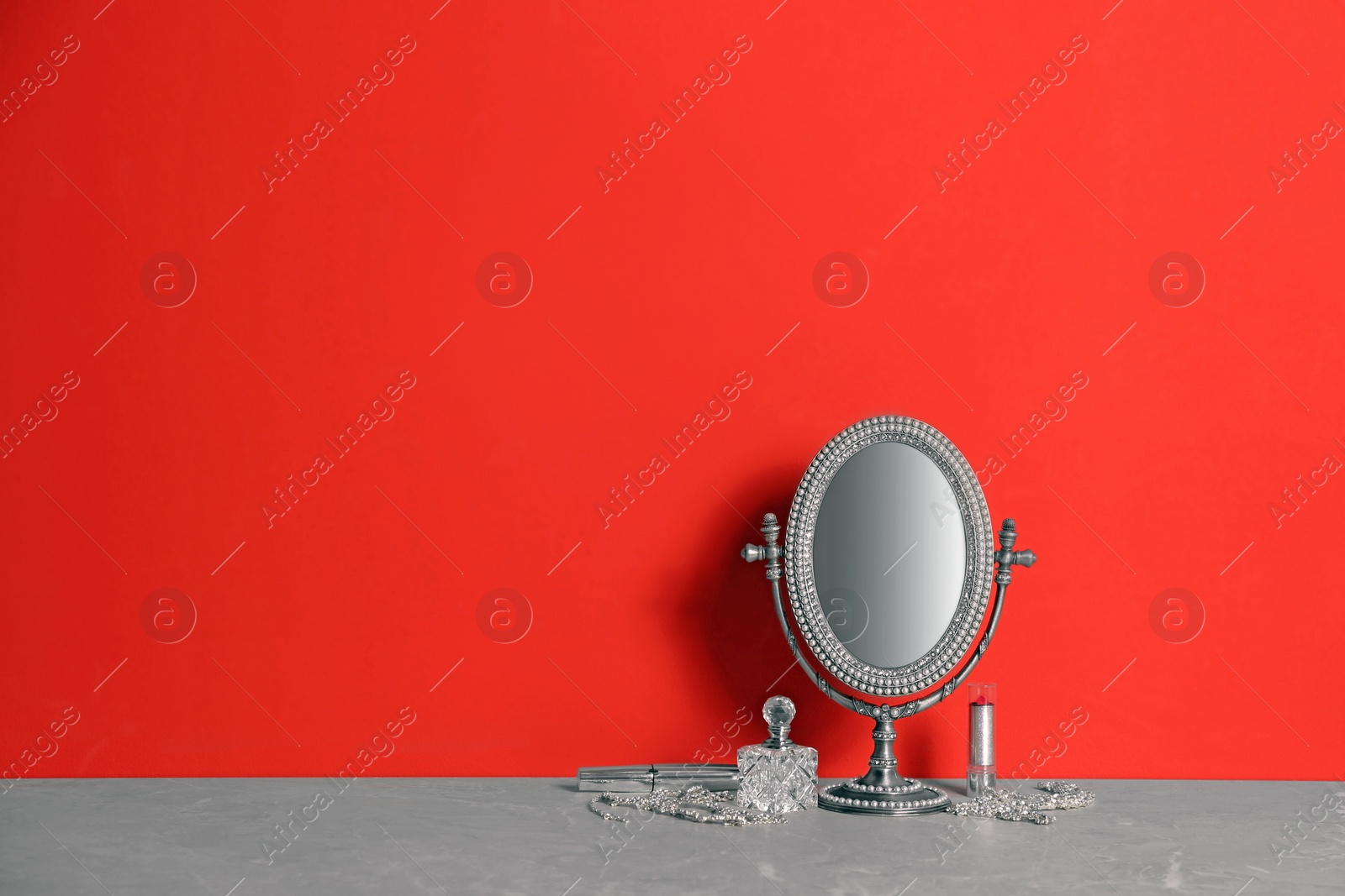 Photo of Small mirror, makeup products and jewelry on grey marble table near red wall. Space for text