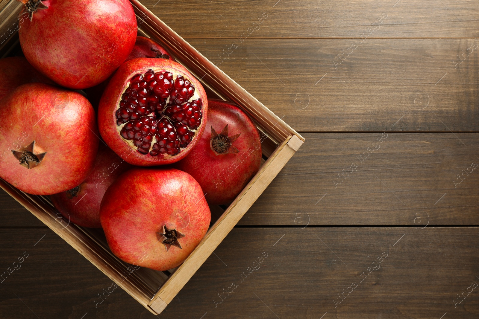 Photo of Ripe pomegranates in crate on wooden table, top view. Space for text