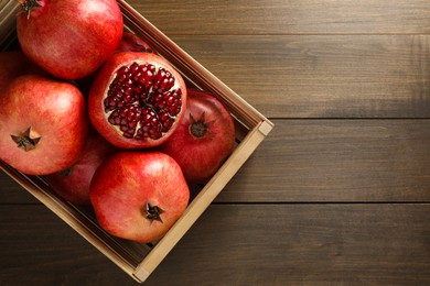 Ripe pomegranates in crate on wooden table, top view. Space for text