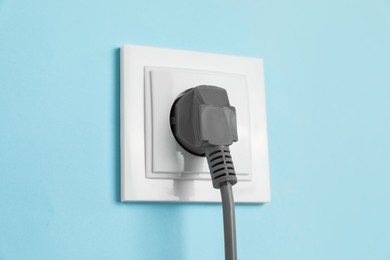 Photo of Power socket with inserted plug on light blue wall, closeup. Electrical supply