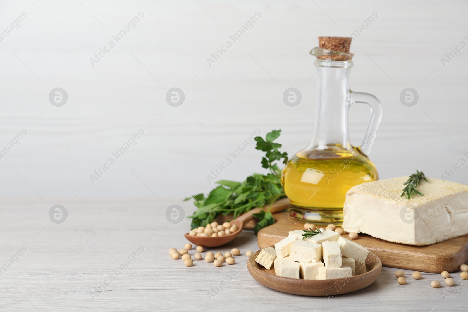 Photo of Pieces of delicious tofu with herbs, oil and soy on white table. Space for text