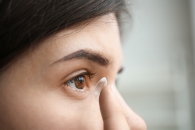 Young woman putting contact lens in her eye on light background, closeup
