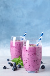 Glasses of tasty blueberry smoothie on white wooden table, space for text