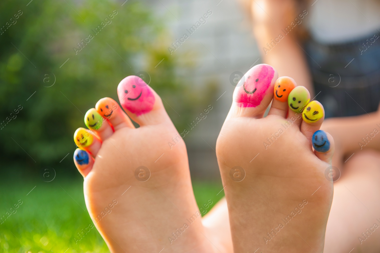 Photo of Teenage girl with smiling faces drawn on toes outdoors, closeup