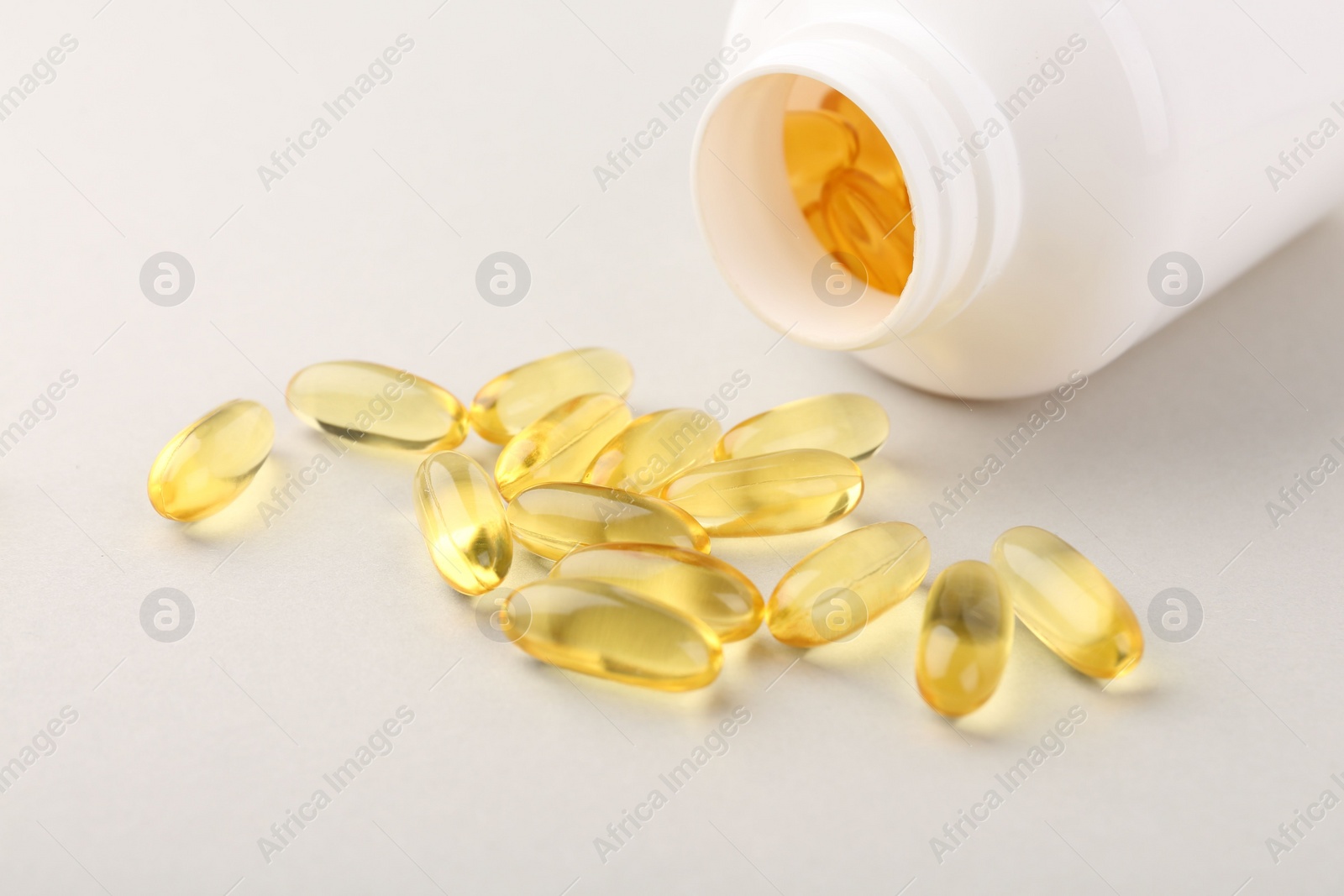 Photo of Vitamin capsules and bottle on light grey background, closeup