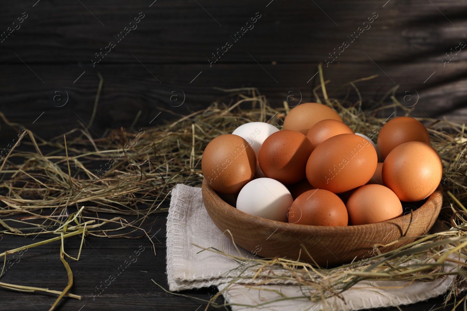 Photo of Fresh chicken eggs in bowl and dried hay on black wooden table. Space for text