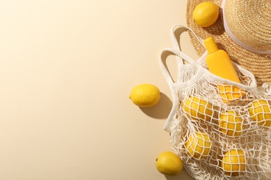 Photo of String bag with fresh lemons, sunscreen and straw hat on beige background, flat lay. Space for text