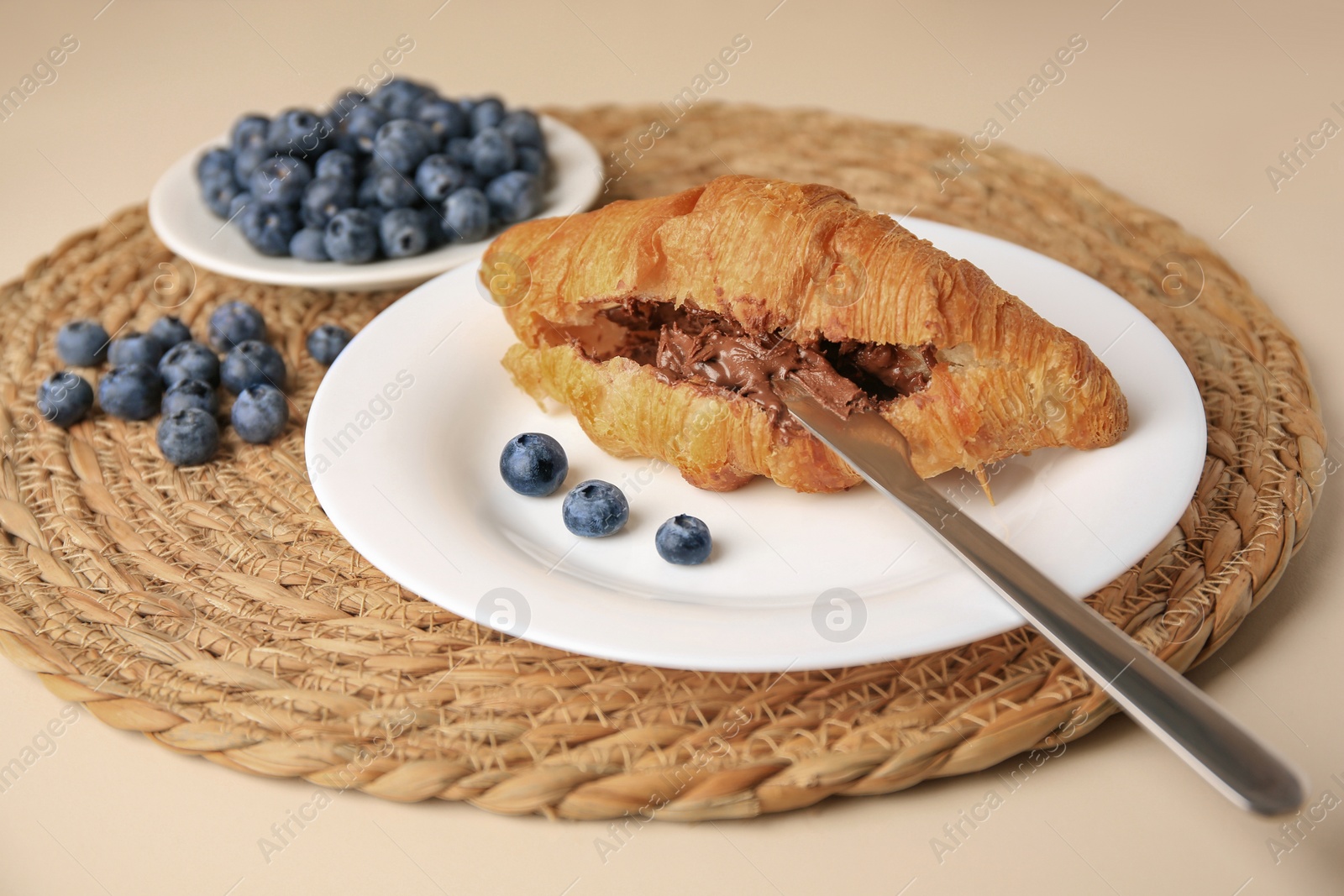 Photo of Tasty croissant with chocolate paste and blueberries on beige background