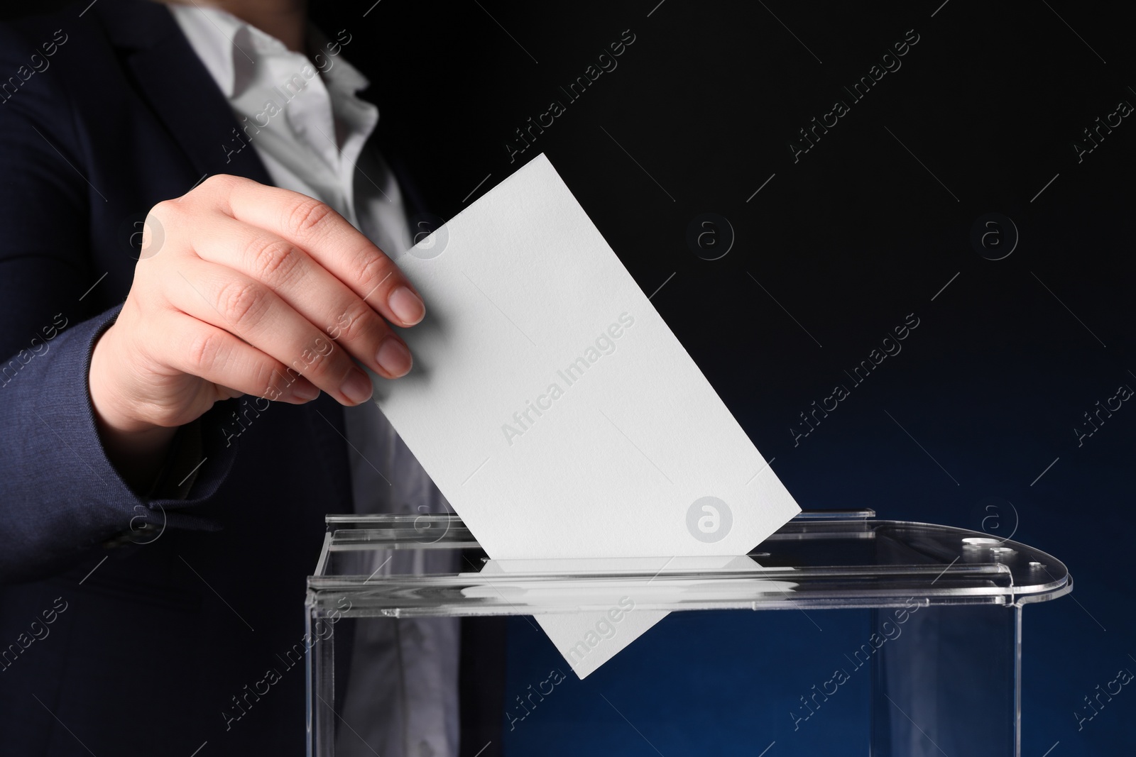 Photo of Woman putting her vote into ballot box on dark blue background, closeup