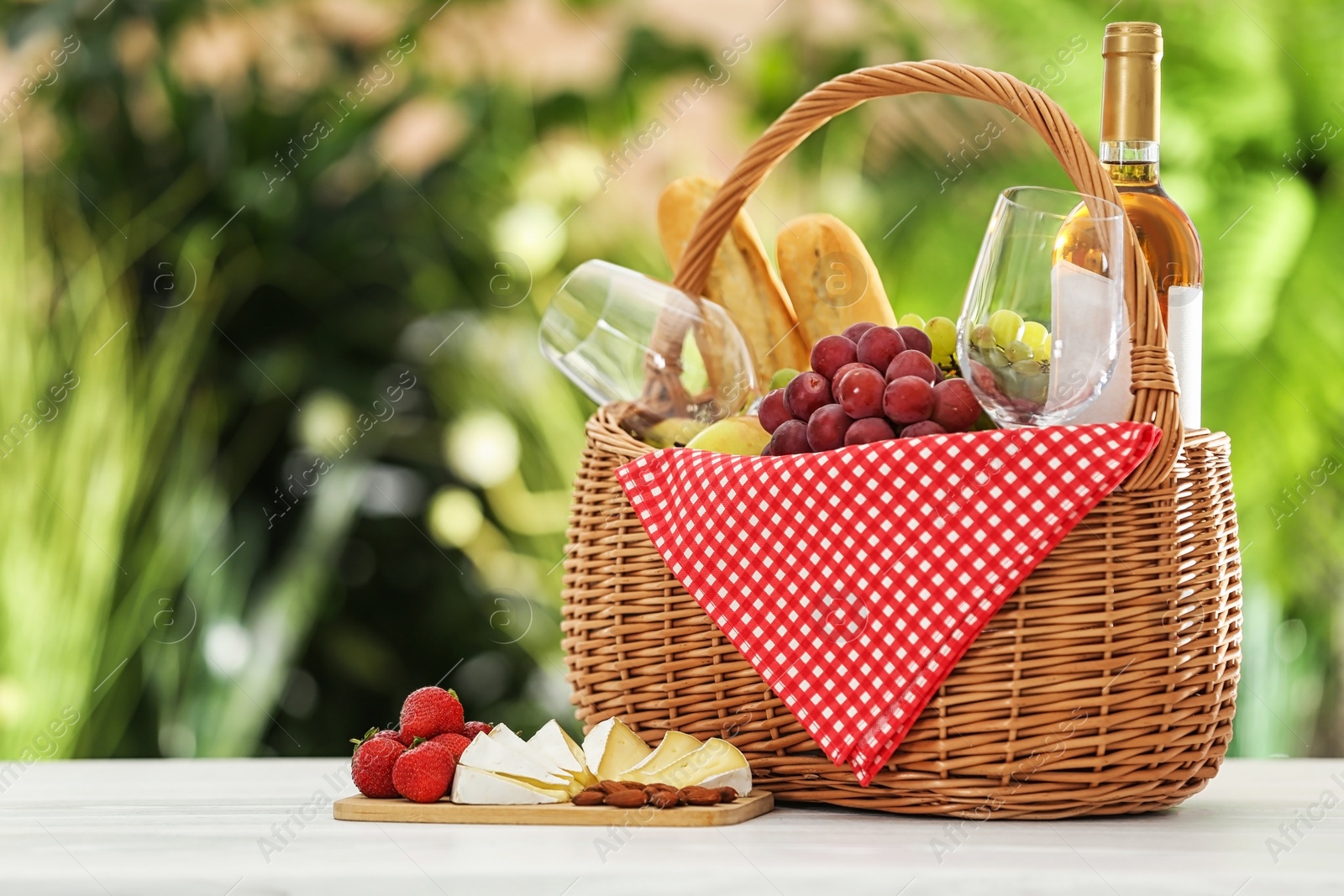 Photo of Picnic basket with products and wine on table against blurred background, space for text