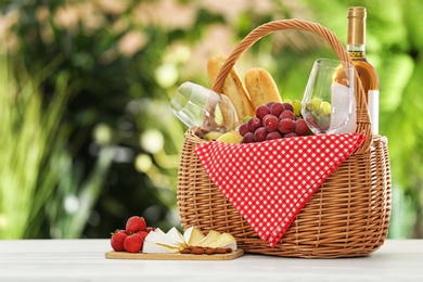 Picnic basket with products and wine on table against blurred background, space for text