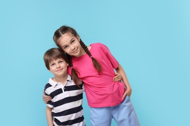 Happy brother and sister hugging on light blue background